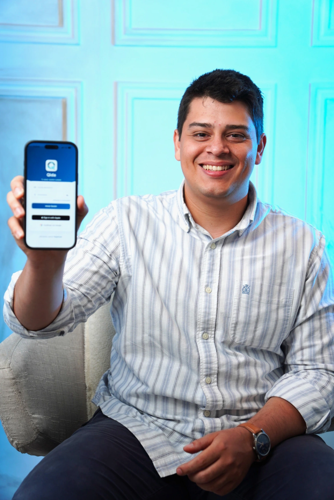 Joseph Corona sonríe y muestra un teléfono con Qida en la mano.